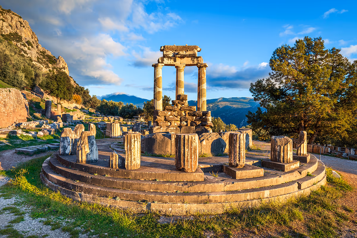 Antike runde Steinplattform mit Säulenruinen vor Berglandschaft unter blauem Himmel.